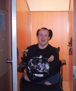 Woman with shorten arms and no legs smiling while getting out of an elevator.