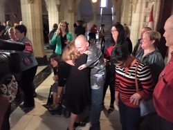 Two thalidomide survivors hugging and other very happy people at a press conference in the Parliament of Canada